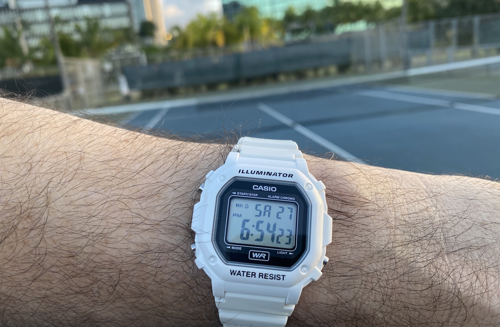 نمایی از ساعت کاسیو Illuminator مربعی سفید روی مچ دست در زمین تنیس