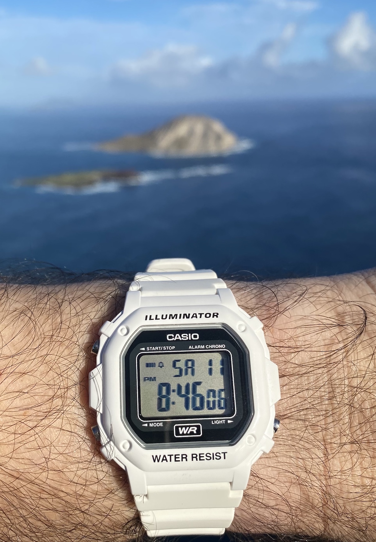 ساعت کاسیو دیجیتال مربعی سفید Illuminator روی مچ دست با پس‌زمینه جزیره