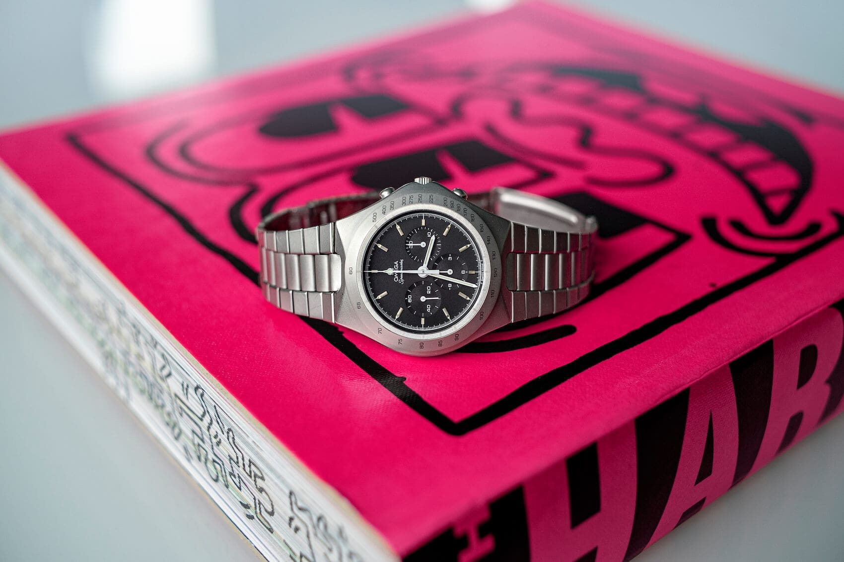 ساعت امگا اسپیدمستر توتونیک کنار کتابی با طرح‌های کیت هرینگ